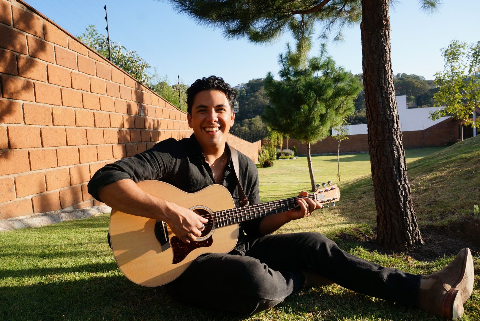 Bernardo Quintero sentado en el pasto, tocando la guitarra